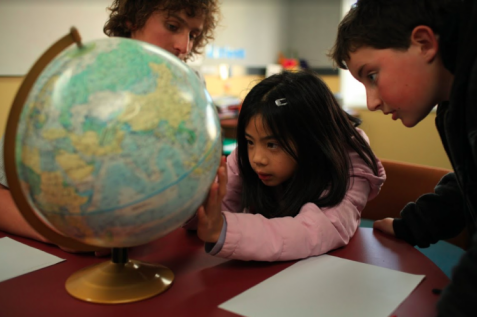 Students and teacher looking at a globe.