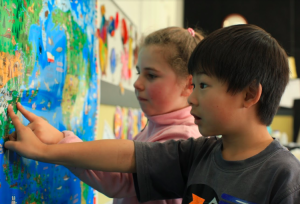 Students pointing to a world map.
