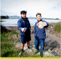 Two boys standing at the edge of an estuary show rubbish they have collected.